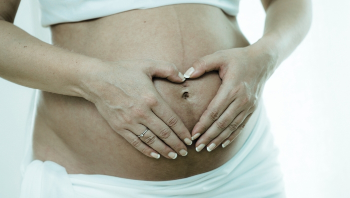 A pregnant person gently forms a heart shape with their hands over their belly—symbolizing connection, care, and the nurturing support of pregnancy massage.